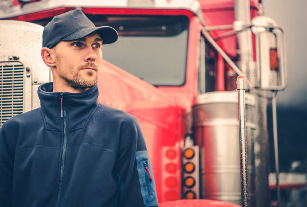 Male truck driver standing in front of semi.