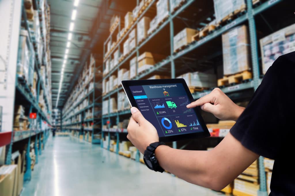 A warehouse with a logistics employee holding an iPad tracking all of the inventory and supply.