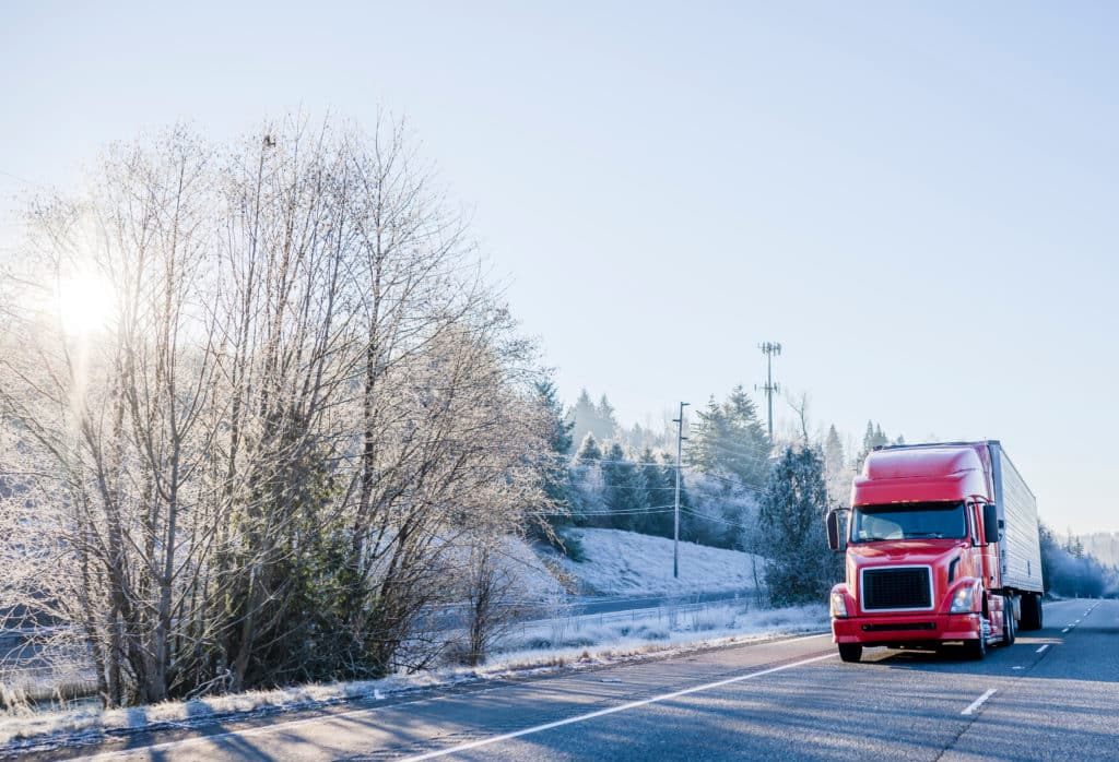 A red truck driving on a road in the winter.