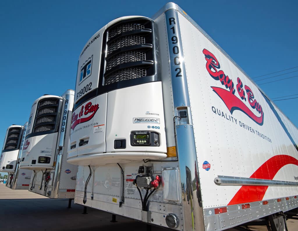 A photo of a line of three Bay & Bay refrigerated trucking trailers.