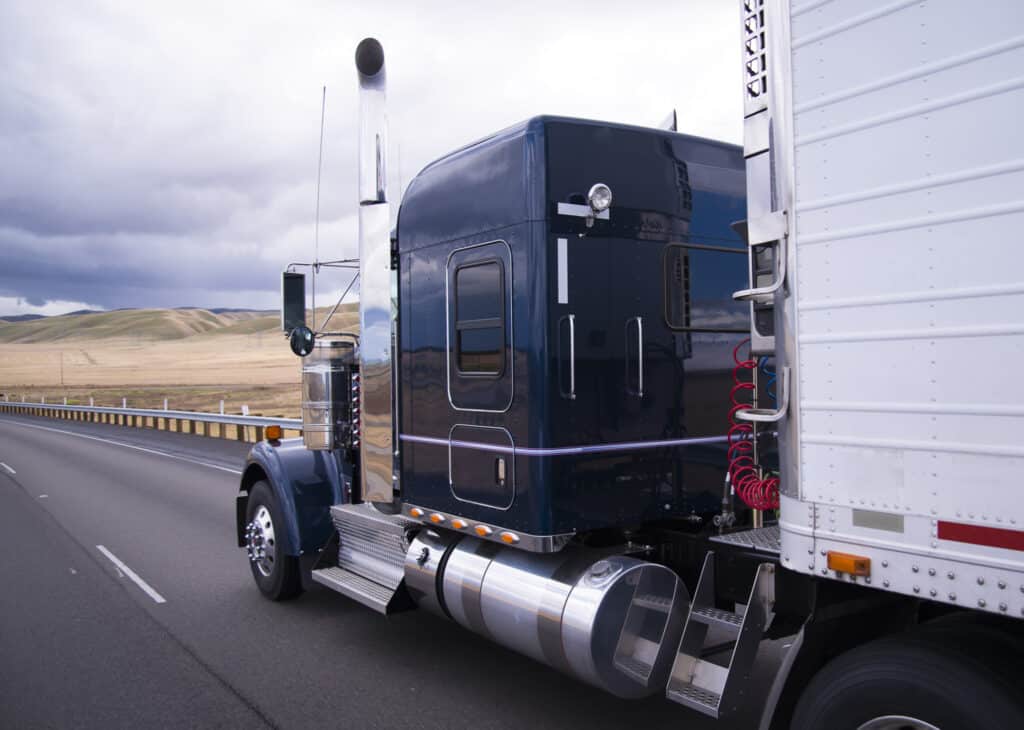 A black truck with a trailer attached driving on the road with open fields around it.