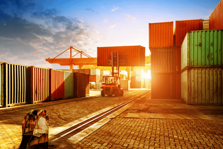 A photo of a 40-foot shipping container transport facility. There is a forklift moving the 40-foot shipping containers to their correct location.